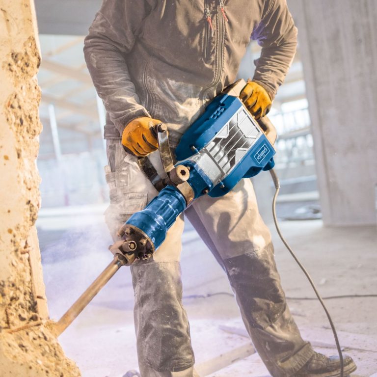 Handwerker mit einem elektrischen Meißel, der eine Wand bearbeitet.