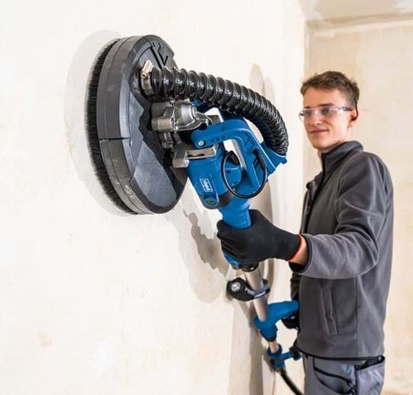 Ein Handwerker schleift eine Wand mit einem elektrischen Schleifgerät.