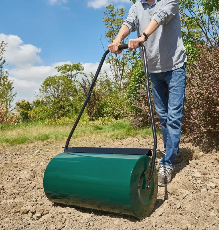 Person, der eine grüne Gartenwalze auf einem Feld schiebt, um den Boden zu ebnen.