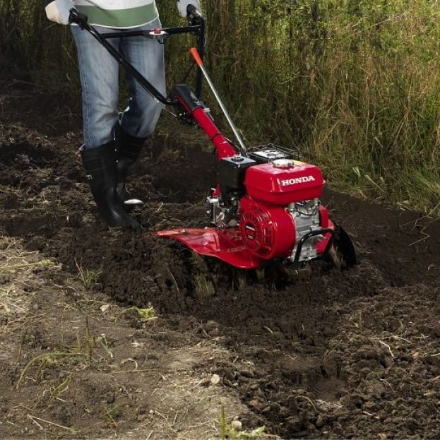 Person mit einer motorisierten Bodenbearbeitungsmaschine in einem Garten.