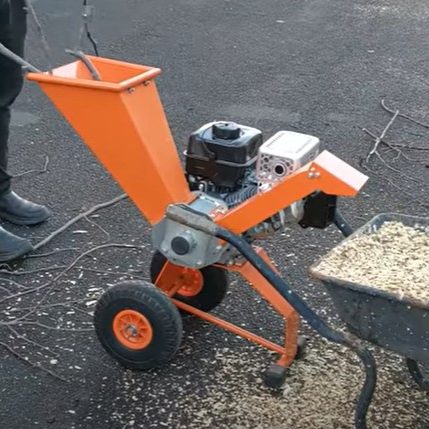 Häcksler in Orange mit Motor, auf einer asphaltierten Fläche, umgeben von Holzspänen.